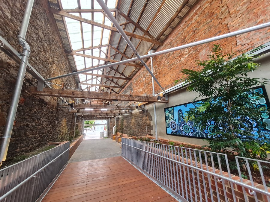 Building interior with exposed bricks, timber roof trusses, and opaque roof sheets bringing light into the large open laneway