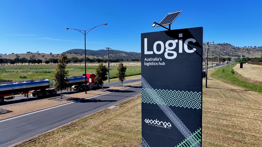 The black, white and green Logic sign, with a solar powered light sitting atop the structure. To the left of the sign a truck can be seen travelling along the adjacent road.