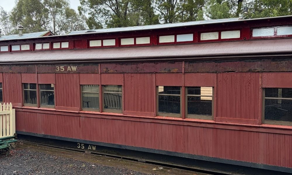 Side-on view of the brown heritage train carriage, with windows and ‘35 AW’ visible. The carriage is stationary on a section of track, also bearing the ‘35 AW’ stamp.