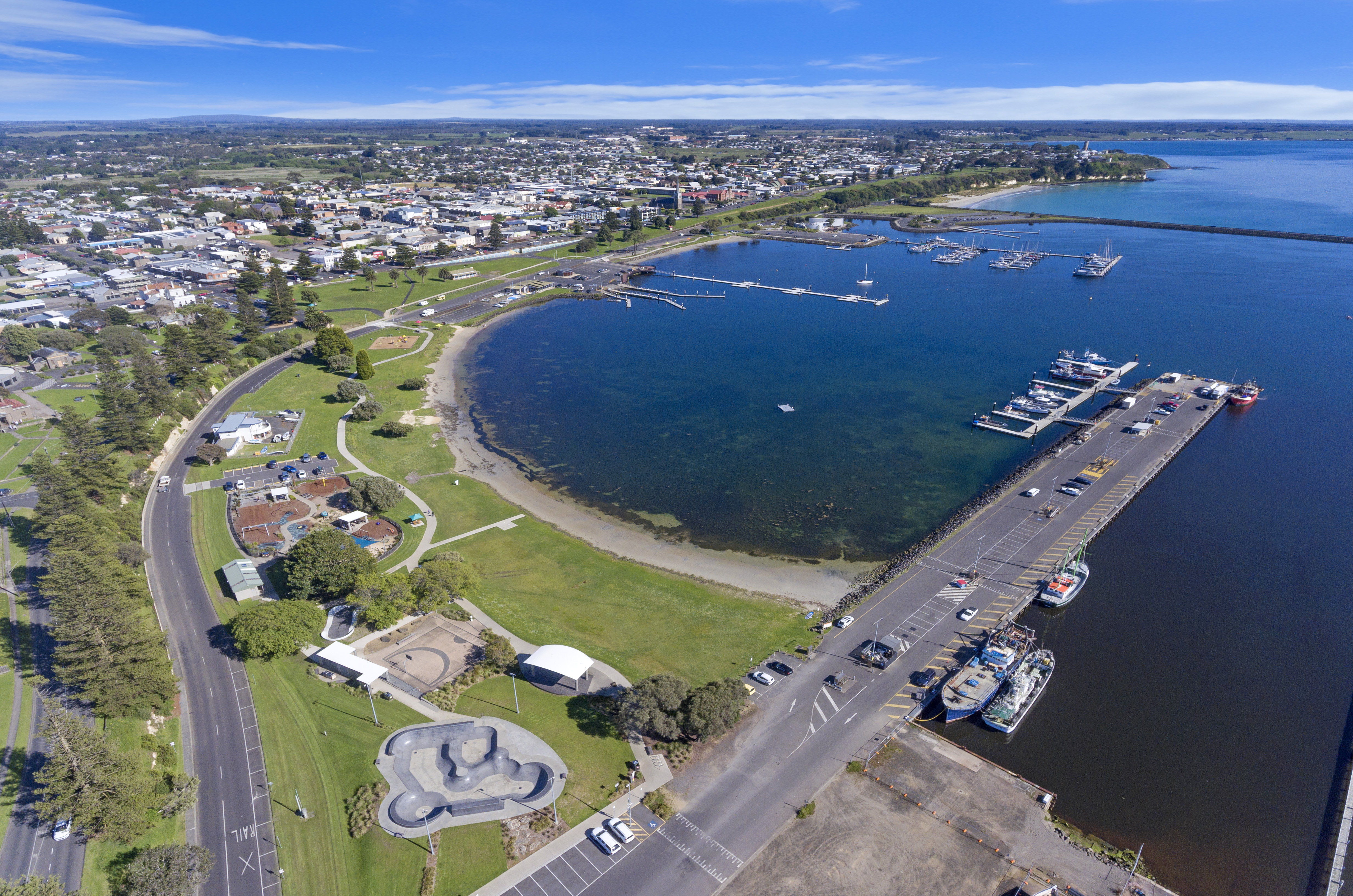The Portland Foreshore. Aerial view of a coastal town waterfront featuring a sheltered harbour with a marina, fishing boats and a long pier.