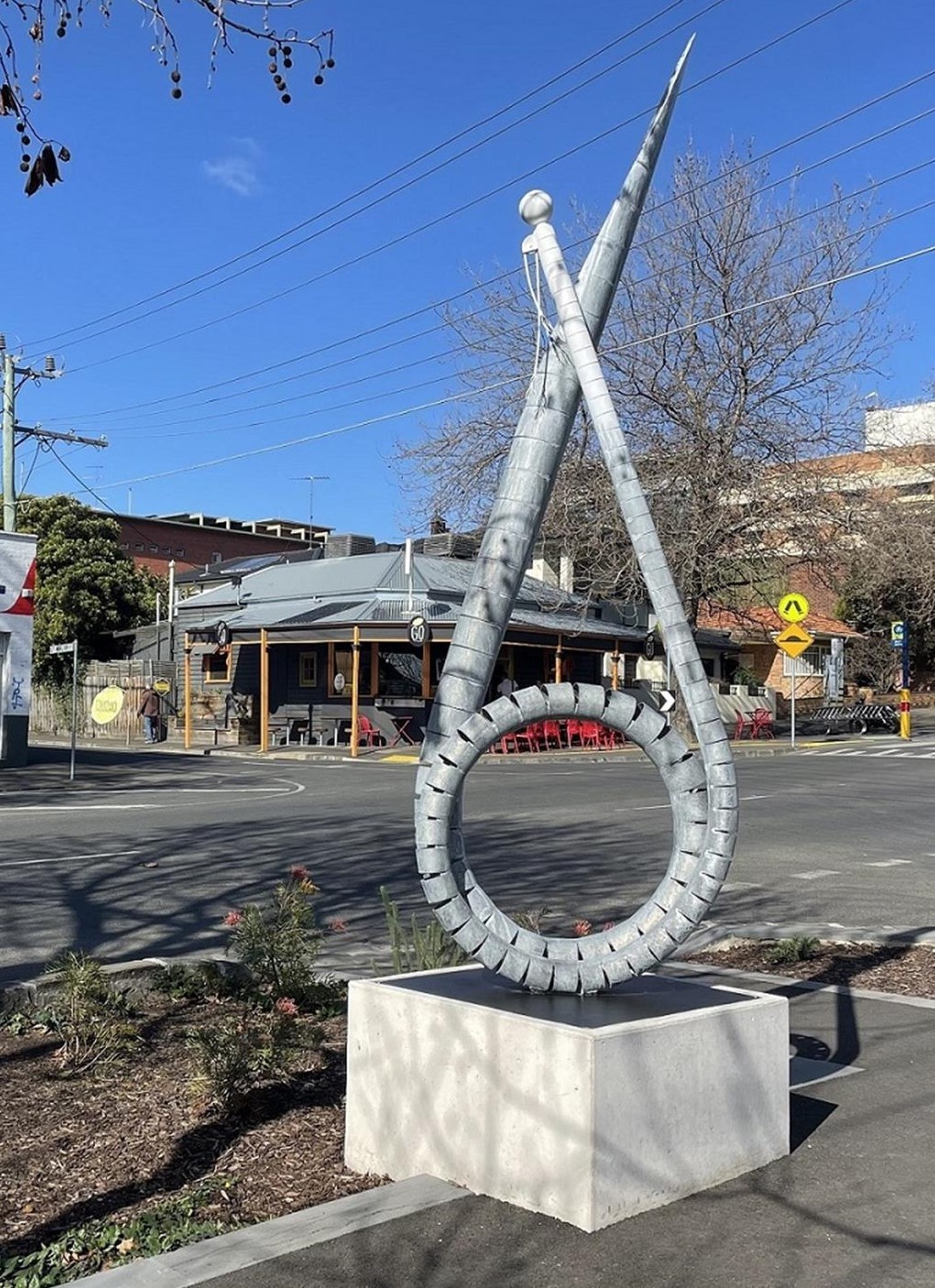 A large sculpture, metalic and coiled stands upright on a concrete platform along the art installation along the Bellerine Street