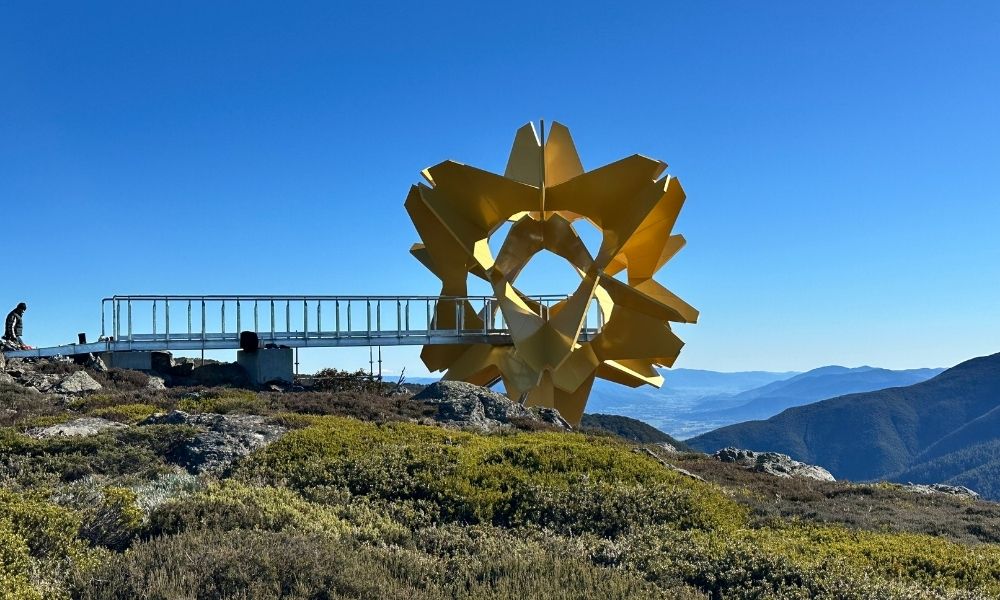 The side view of the Flower of the Alpine Sun sculpture, which can be seen sitting atop Falls Creek with mountain peaks and a valley in the background.