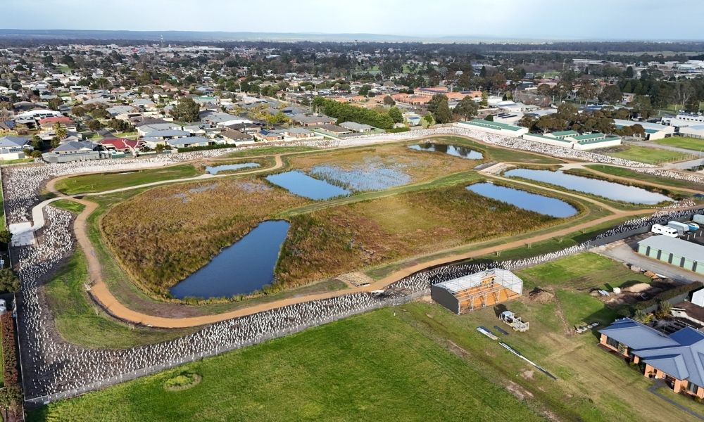 Drone view of the wetlands and biodiversity reserve. Set in a greenspace that’s surrounded by houses, the image shows 7 large ponds surrounded by marshland, an ovular walking track and hundreds of newly planted trees.