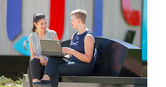 Two women sitting on a bench looking at a computer