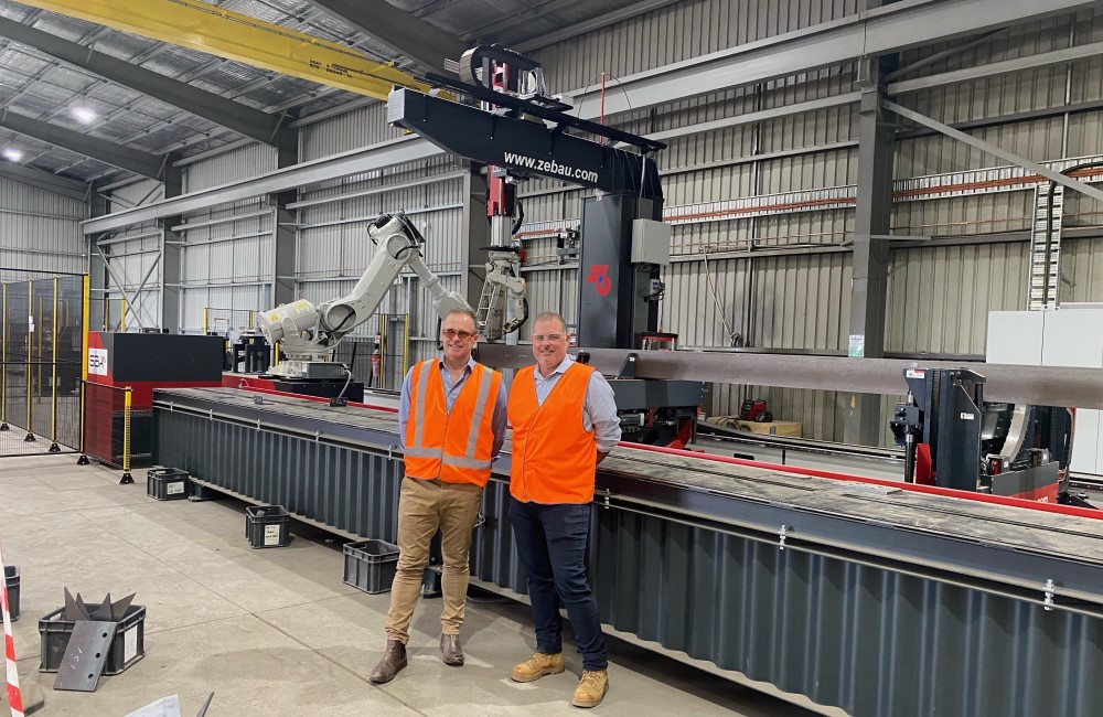 Two people in hi-vis standing in front of robotic assembly unit in factory.