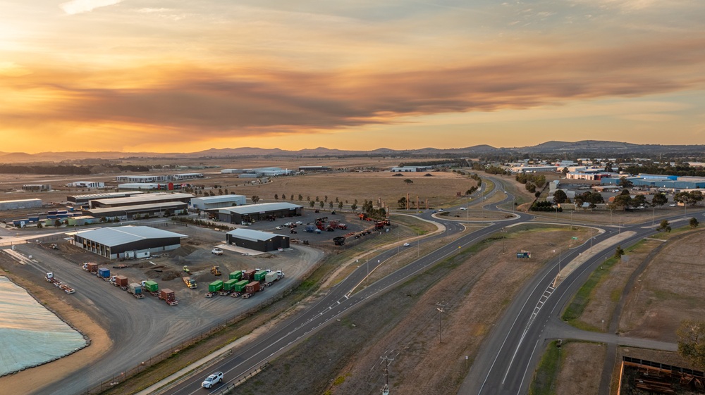 Drone shot of the Ballarat West Employment Zone, with industrial buildings visible in the left and top right of the frame, while a road with cars runs through the middle of the photo. Taken at dusk, the image features an orange hue coloured by the sunset.