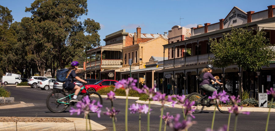 Two cyclists riding through a street in Castlemaine with heritage buildings in the background.
