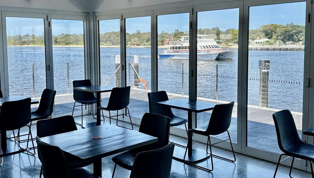 Cafe seating overlooking a lake with a boat driving past.