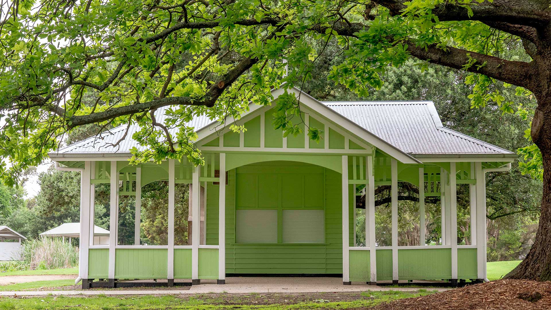 A green weatherboard pavilion under a tree.