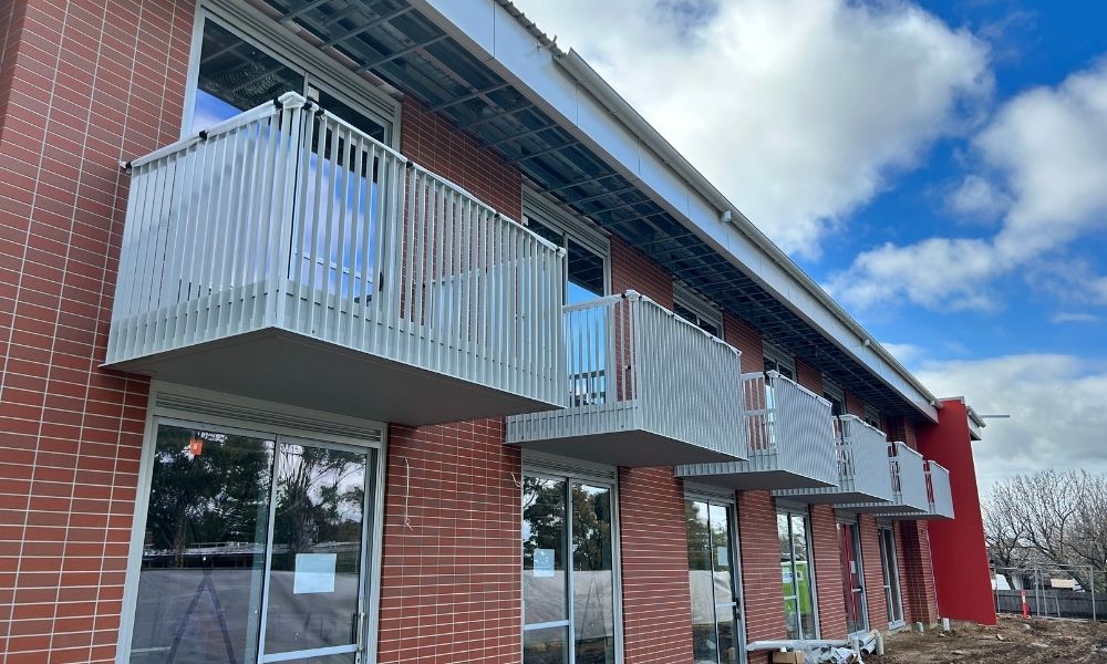 The exterior of the new apartment-style accommodation in Bairnsdale. The building is red brick, with six white balconies visible on the second floor windows. The building is surrounded by dirt, as it is still an active construction site.