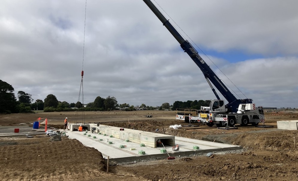 Large concrete slab in dirt field with craner lowering concrete items.