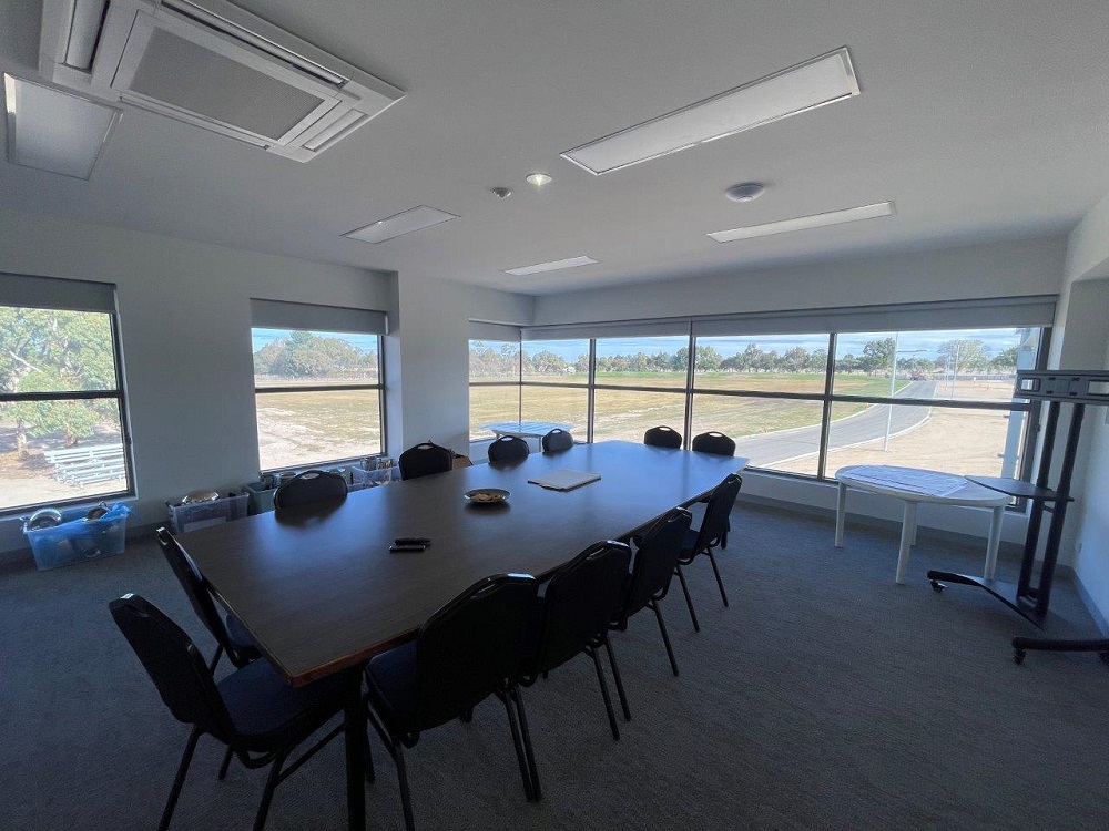 Meeting room at the new Mount Rowan Showgrounds, with a long wooden table in centre shot, surrounded by chairs, overlooking the road entrance to the showgrounds through the back window. 