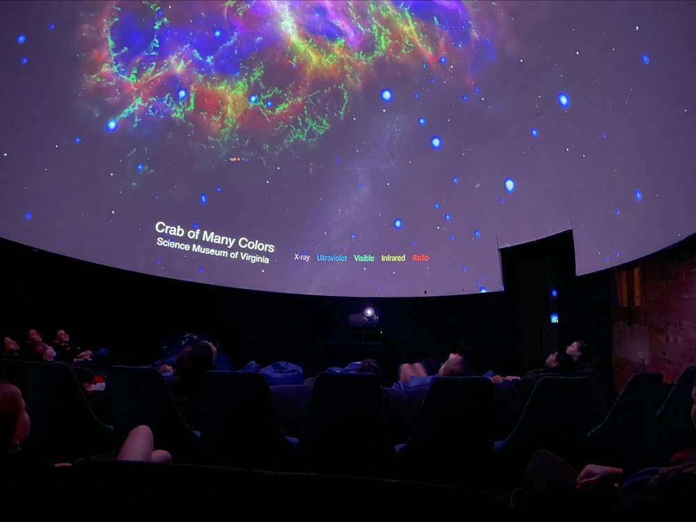 A demonstration of the dome with Crab of many colours galaxy projected on the dome with a group of people in reclined seats looking up at the dome like a night sky