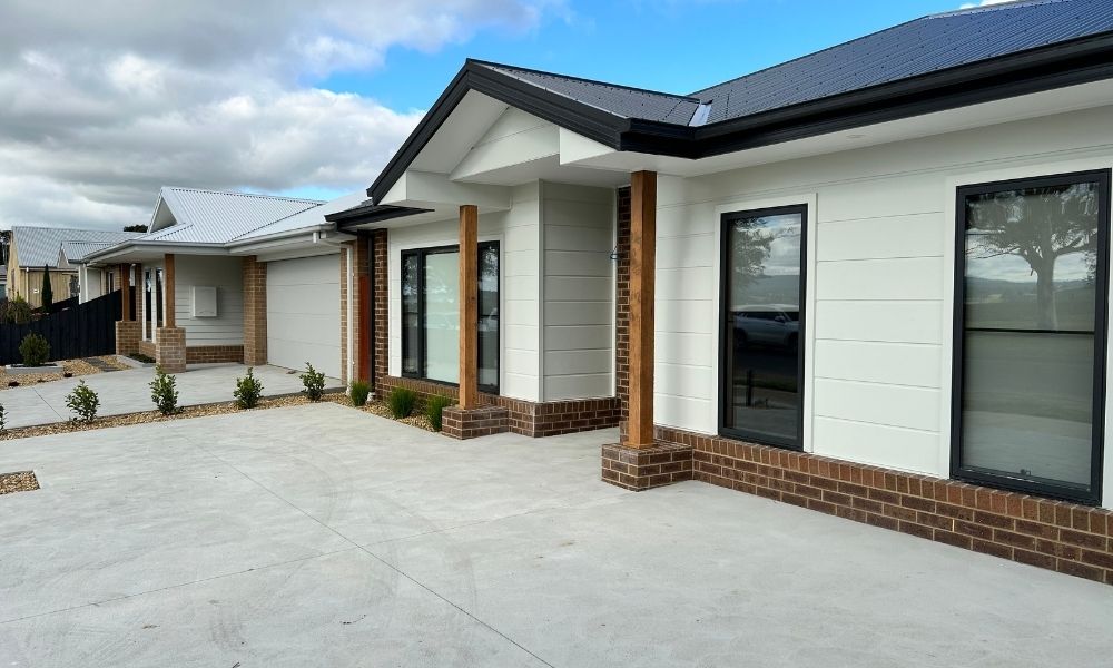 The completed exterior of the Riviera Fresh housing. The house closest to camera on the right of the image has white walls and a black roof, and the house furthest from the camera on the left has white walls and a white roof. Both houses have a walk-up concrete driveway.