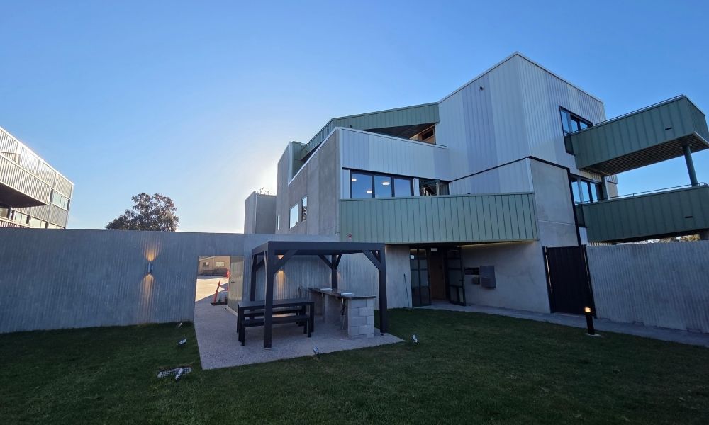 The new GV Health worker accommodation, which is a multi-storey, concrete building with self-contained units, each featuring a balcony with green fencing that overlook the shared-use barbecue and lawn area.