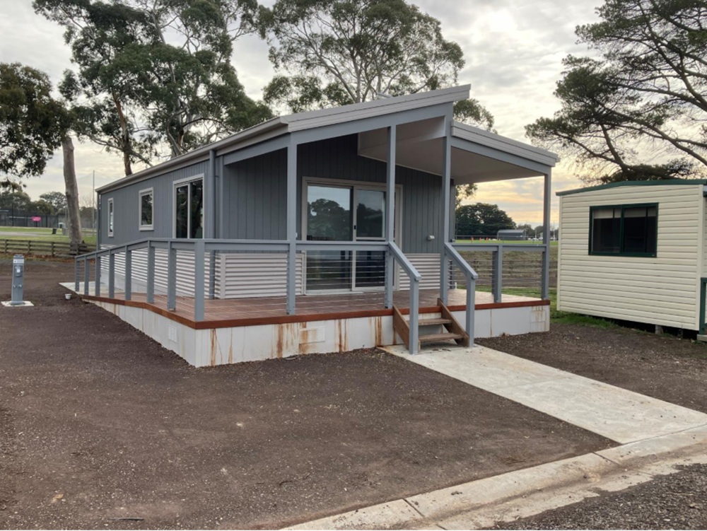 The park’s new all-abilities cabin, featuring ramp access to the left side of the building and small stairs at the front. The cabin has blue walls and veranda support beams, with a short white pathway leading to the entrance. 